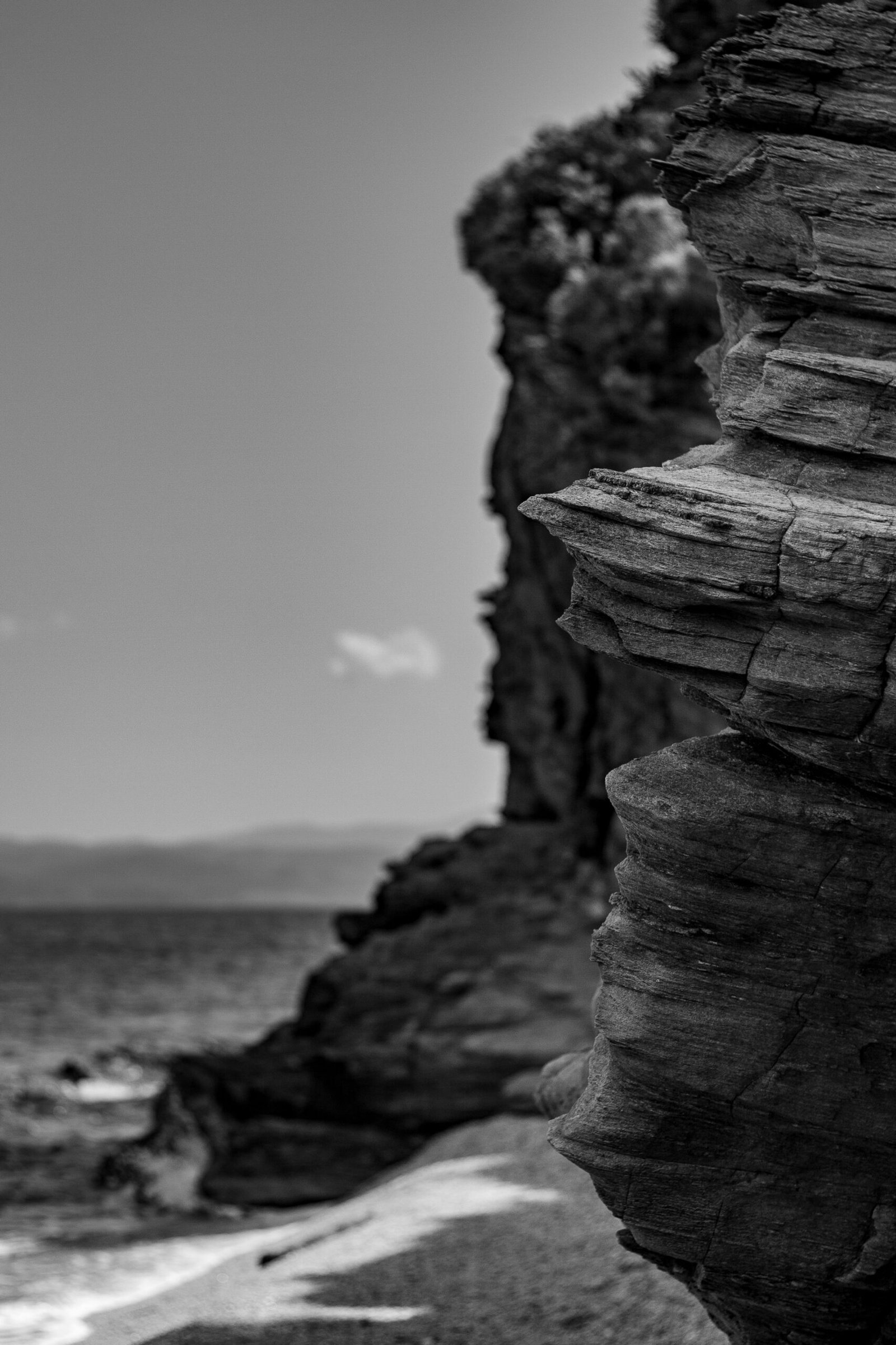 grayscale photo of rocky mountain near body of water